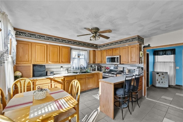 kitchen with sink, light tile patterned floors, kitchen peninsula, ceiling fan, and stainless steel appliances