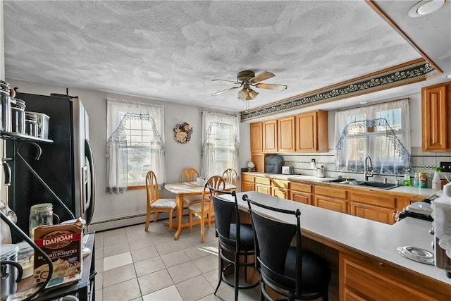 kitchen featuring sink, light tile patterned floors, ceiling fan, backsplash, and a baseboard radiator