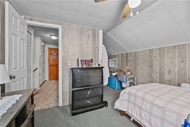 bedroom with ceiling fan, carpet flooring, vaulted ceiling, and wood walls