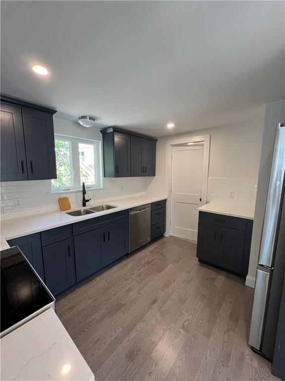 kitchen with tasteful backsplash, sink, stainless steel appliances, and light wood-type flooring