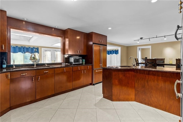 kitchen with paneled refrigerator, sink, light tile patterned floors, and dark stone counters