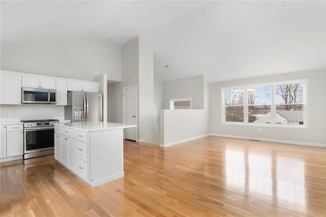 kitchen featuring white cabinetry, high vaulted ceiling, light wood-type flooring, appliances with stainless steel finishes, and a kitchen island