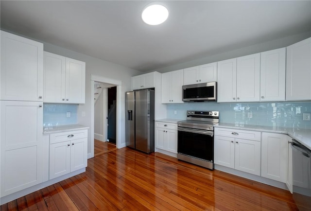 kitchen with white cabinetry, stainless steel appliances, hardwood / wood-style floors, and backsplash