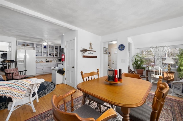 dining room featuring ceiling fan, washer / dryer, light hardwood / wood-style flooring, and a textured ceiling