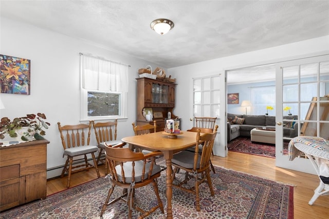 dining area with a baseboard radiator, hardwood / wood-style floors, a textured ceiling, and french doors