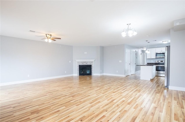 unfurnished living room with a tiled fireplace, ceiling fan with notable chandelier, and light hardwood / wood-style flooring