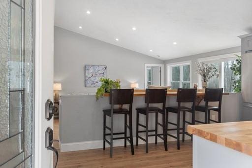 interior space featuring wood-type flooring, butcher block counters, a breakfast bar, and vaulted ceiling