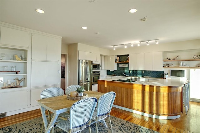 kitchen with tasteful backsplash, light wood-type flooring, kitchen peninsula, stainless steel appliances, and white cabinets