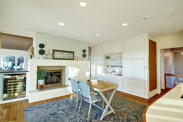 dining space featuring wine cooler, dark wood-type flooring, and a large fireplace