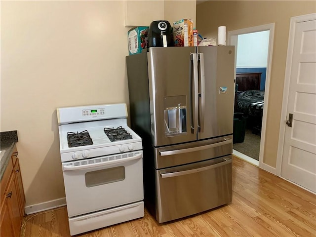 kitchen with white range with gas cooktop, stainless steel fridge, and light wood-type flooring