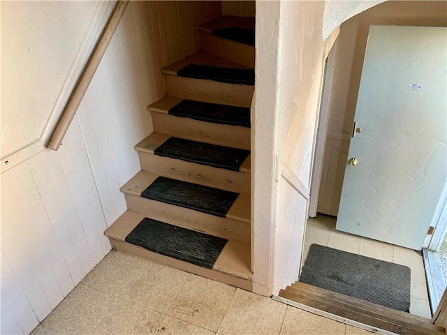 staircase with tile patterned floors and wood walls