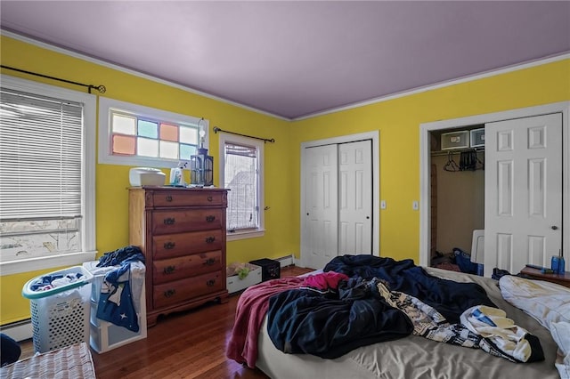 bedroom featuring baseboard heating, ornamental molding, hardwood / wood-style floors, and two closets