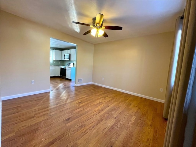 empty room with a ceiling fan, baseboards, visible vents, and wood finished floors