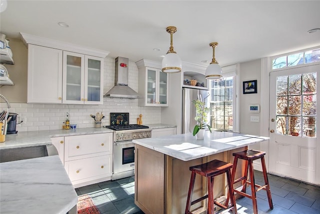 kitchen featuring white cabinetry, a center island, light stone counters, stainless steel appliances, and wall chimney range hood