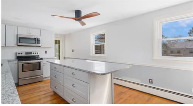 kitchen featuring a center island, appliances with stainless steel finishes, ceiling fan, light hardwood / wood-style floors, and a baseboard heating unit