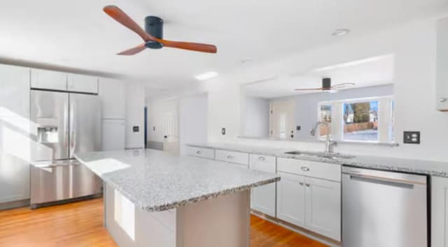 kitchen featuring sink, stainless steel appliances, light stone counters, light hardwood / wood-style floors, and a kitchen island