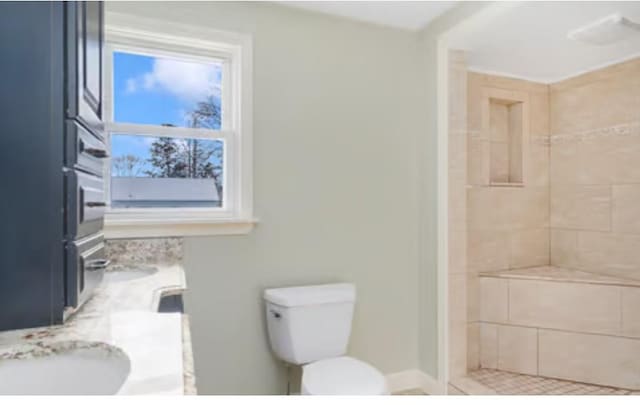 bathroom featuring vanity, a tile shower, and toilet