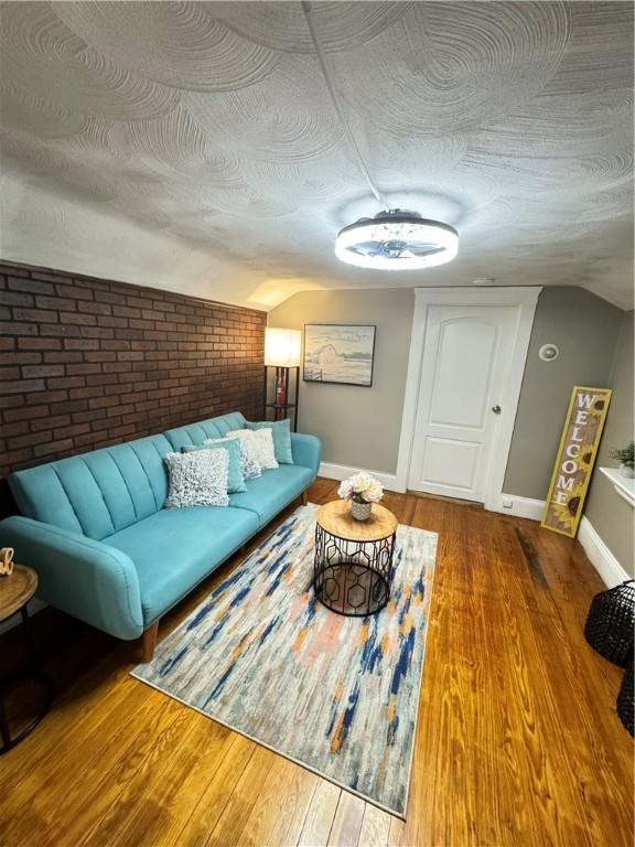 living room featuring brick wall, hardwood / wood-style floors, lofted ceiling, and a textured ceiling