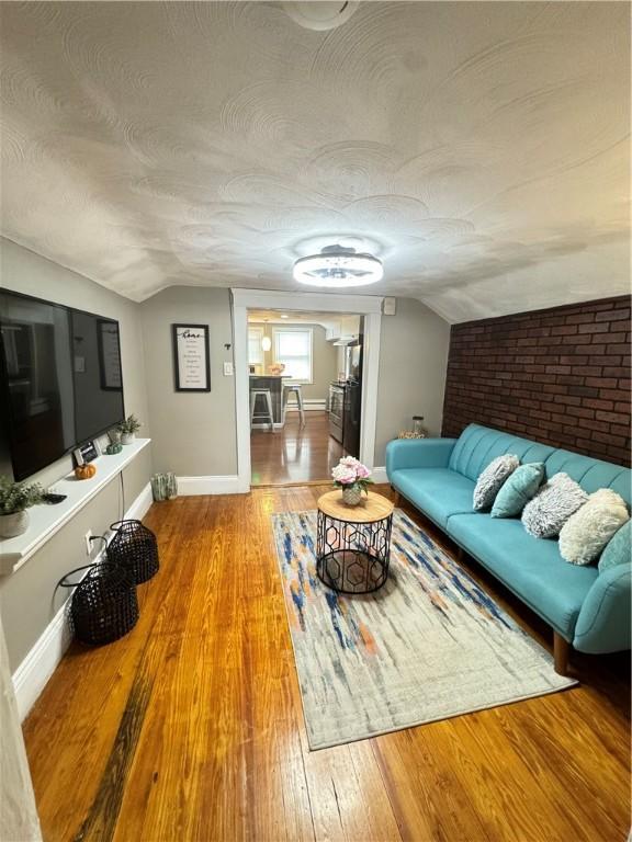 living room with brick wall, lofted ceiling, wood-type flooring, and a textured ceiling