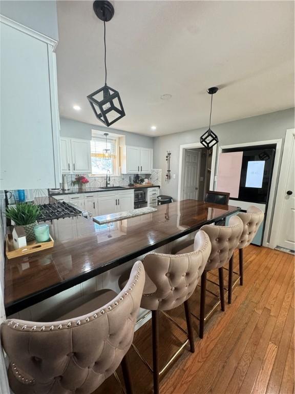 kitchen with tasteful backsplash, sink, white cabinets, and decorative light fixtures