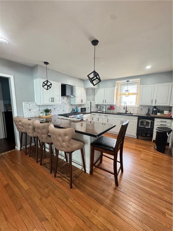 kitchen with white cabinetry, sink, backsplash, hanging light fixtures, and wall chimney range hood