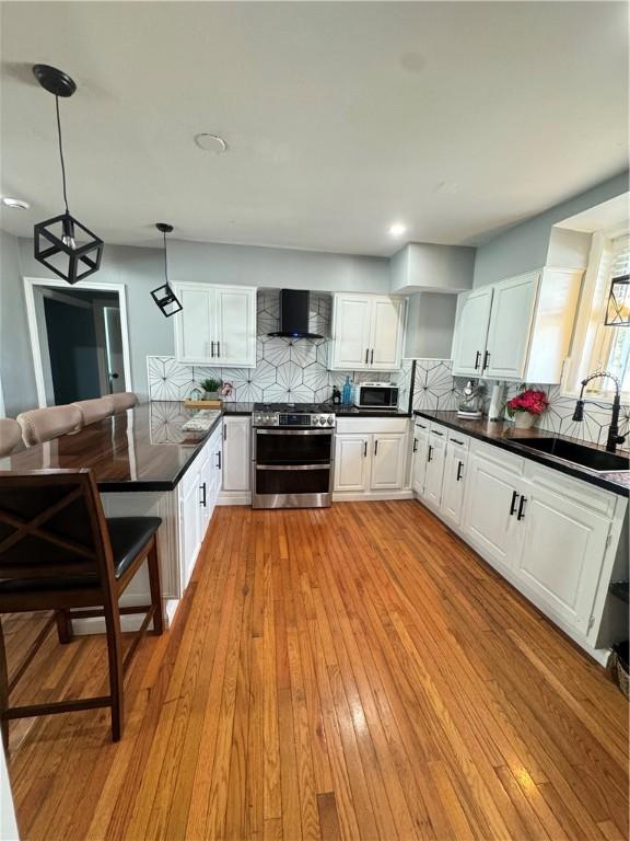 kitchen featuring wall chimney range hood, sink, double oven range, white cabinets, and decorative light fixtures