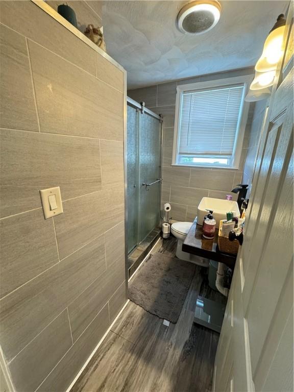 bathroom with toilet, a shower with door, sink, and hardwood / wood-style flooring