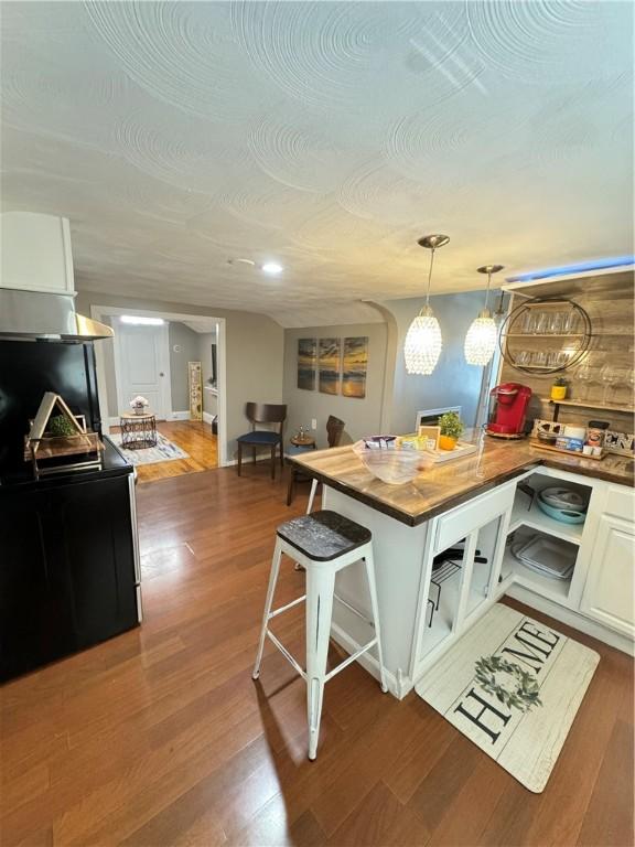 kitchen featuring a breakfast bar, white cabinetry, hanging light fixtures, butcher block counters, and dark hardwood / wood-style floors