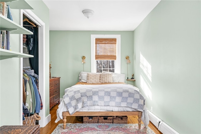 bedroom with a baseboard radiator, hardwood / wood-style floors, and a closet