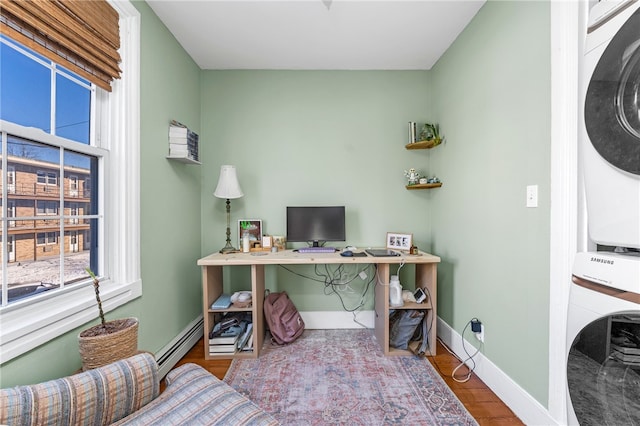 office area with stacked washing maching and dryer, hardwood / wood-style floors, and baseboard heating