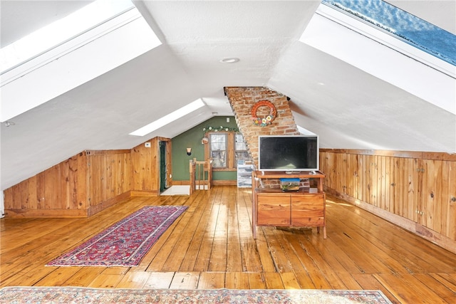 additional living space featuring wood-type flooring, lofted ceiling with skylight, wooden walls, and a textured ceiling