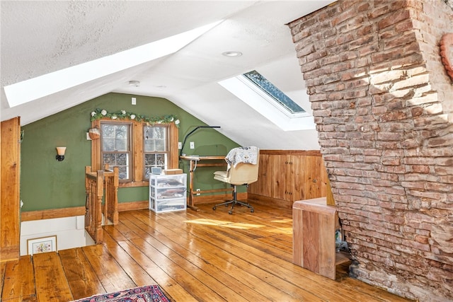 unfurnished office with hardwood / wood-style flooring, vaulted ceiling with skylight, and a textured ceiling