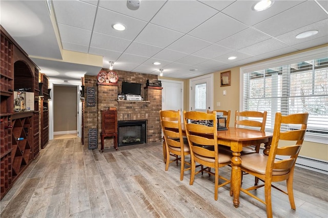 dining space featuring a paneled ceiling, a fireplace, and light hardwood / wood-style flooring