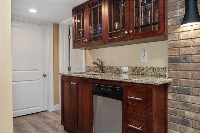 bar featuring sink, light stone counters, light wood-type flooring, dishwasher, and brick wall