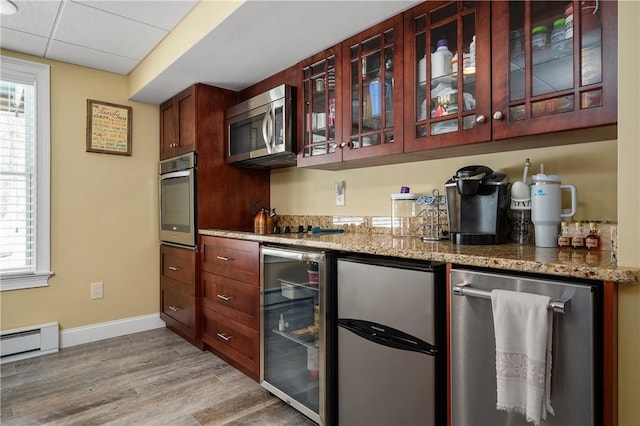 kitchen with a paneled ceiling, stainless steel appliances, wine cooler, light stone counters, and light wood-type flooring