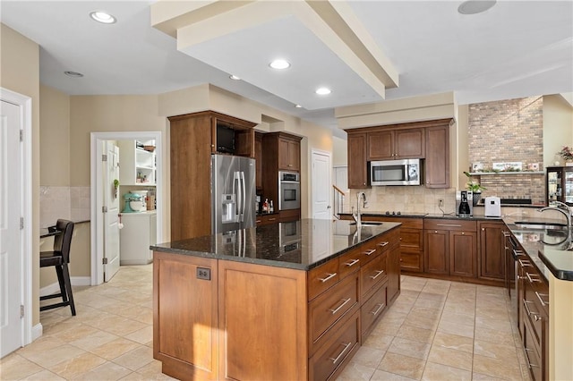 kitchen featuring sink, a center island with sink, light tile patterned floors, appliances with stainless steel finishes, and dark stone counters