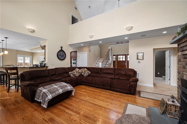 living room with a brick fireplace, light hardwood / wood-style flooring, and high vaulted ceiling