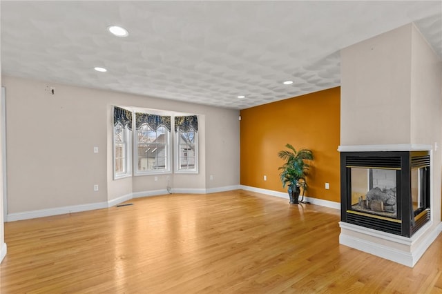 unfurnished living room featuring a multi sided fireplace and light hardwood / wood-style flooring