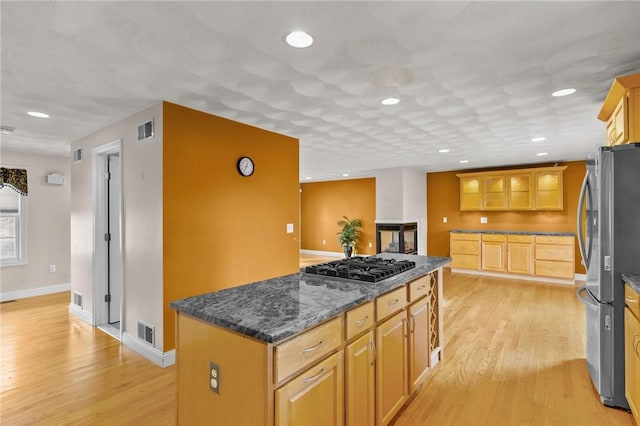 kitchen with stainless steel appliances, a center island, dark stone countertops, and light hardwood / wood-style floors