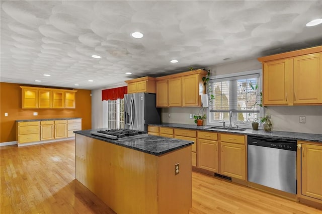 kitchen featuring appliances with stainless steel finishes, sink, dark stone countertops, a center island, and light wood-type flooring