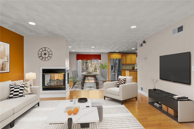 living room featuring a multi sided fireplace and light hardwood / wood-style floors