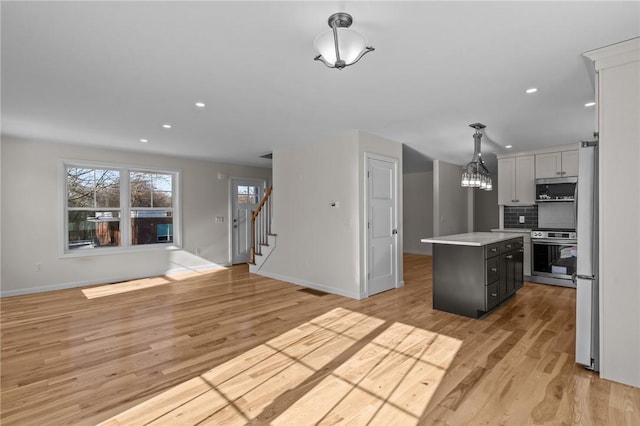 kitchen with pendant lighting, decorative backsplash, a center island, stainless steel appliances, and light wood-type flooring