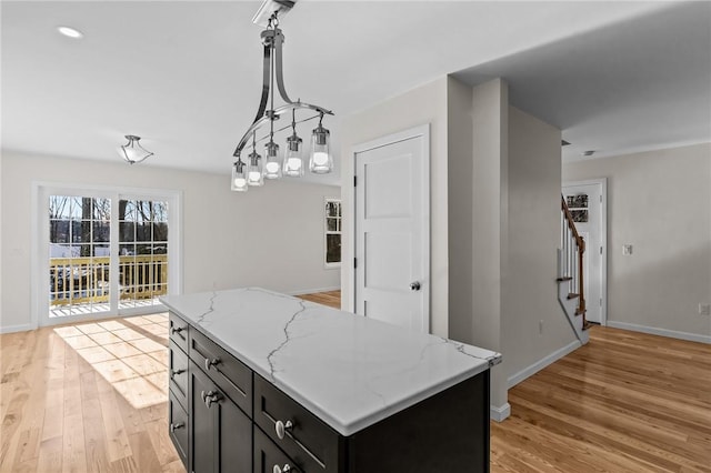 kitchen with light stone countertops, a kitchen island, light wood-type flooring, and decorative light fixtures