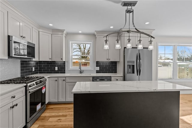 kitchen with pendant lighting, appliances with stainless steel finishes, light stone counters, and a kitchen island