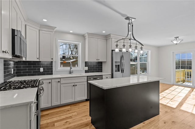 kitchen with a kitchen island, appliances with stainless steel finishes, sink, hanging light fixtures, and light wood-type flooring