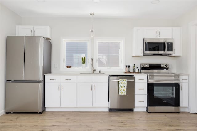 kitchen with pendant lighting, stainless steel appliances, light wood-style flooring, white cabinetry, and a sink