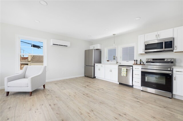 kitchen featuring stainless steel appliances, an AC wall unit, light countertops, and white cabinetry