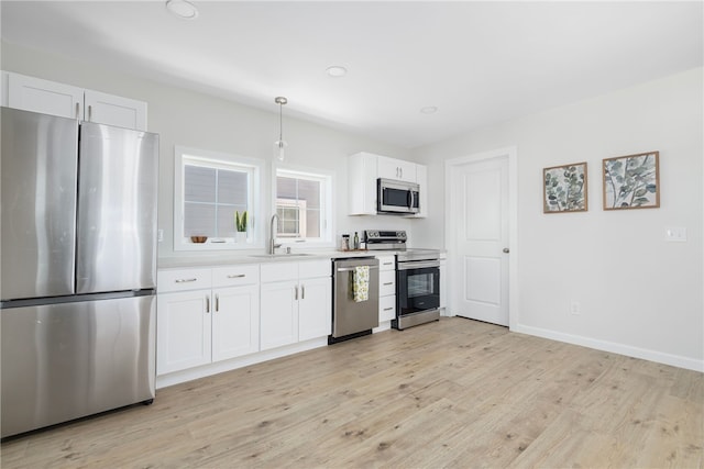 kitchen with stainless steel appliances, light countertops, hanging light fixtures, white cabinetry, and a sink