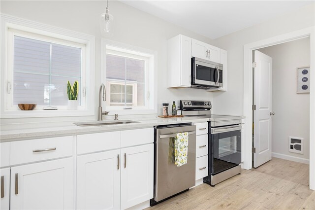 kitchen with stainless steel appliances, a sink, white cabinetry, light wood-style floors, and light countertops