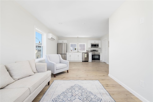 living room with a wealth of natural light, baseboards, light wood-style floors, and an AC wall unit